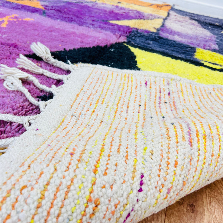Close-up of a vibrant vintage Moroccan rug with sunset colors showcasing purple, yellow, and orange patterns.