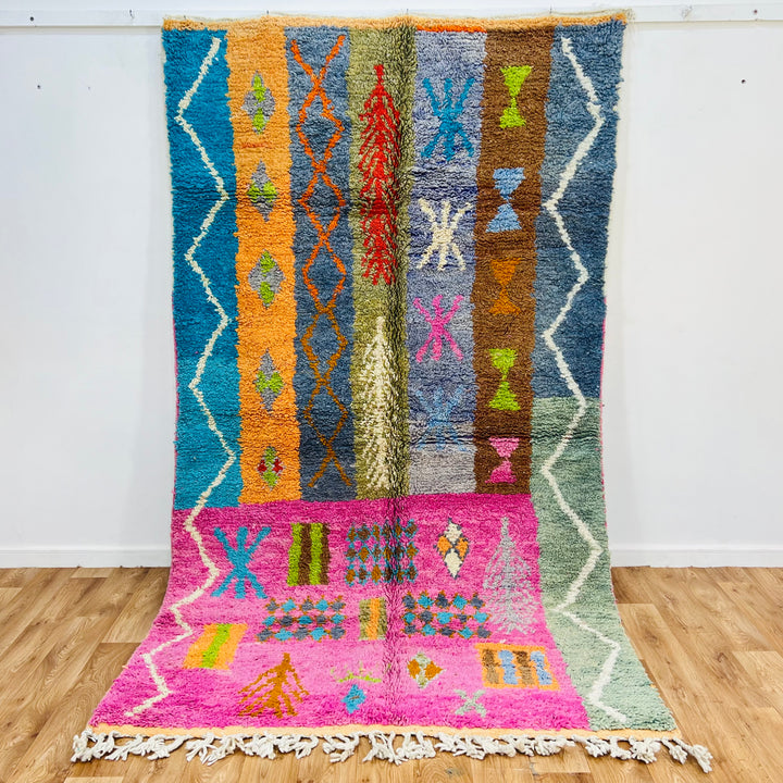 Colorful 9x5 ft Berber Moroccan rug with tribal patterns and symbols on a pink and orange base, handmade wool carpet.
