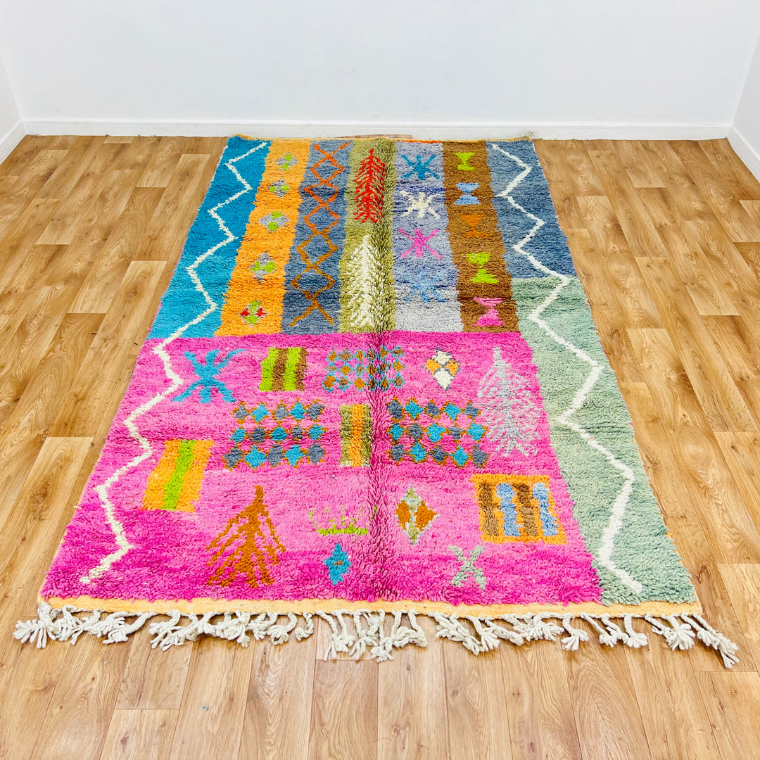 Colorful 9x5 ft Berber Moroccan rug with tribal patterns on a pink and orange base, handmade from premium wool.