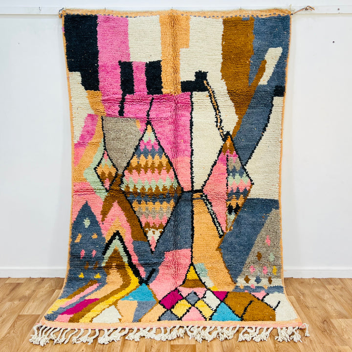 Colorful vintage Moroccan wool rug with geometric diamond patterns and vibrant hues of pink, cream, mustard, blue, and orange.