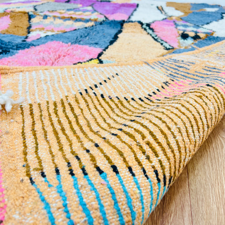 Colorful Moroccan wool rug with geometric diamond design in pink, cream, mustard, blue, and orange hues, 256 x 169 cm.