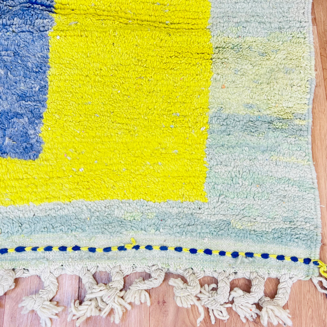 Yellow Moroccan wool rug with abstract design and tribal patterns, featuring blue, green, and yellow hues on a hardwood floor.