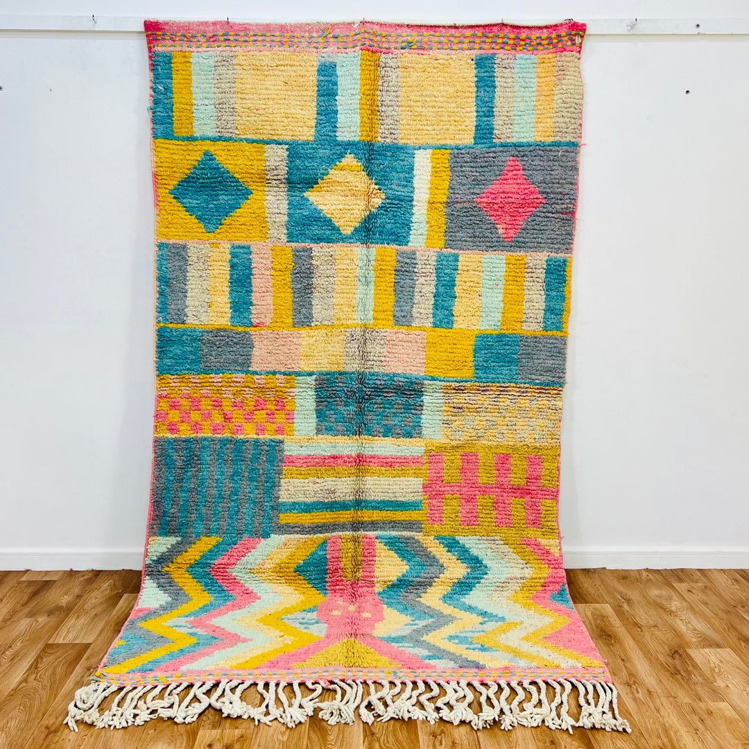 Vintage Moroccan wool rug with colorful Berber design, featuring yellow, pink, teal, and grey geometric patterns, handwoven in wool.