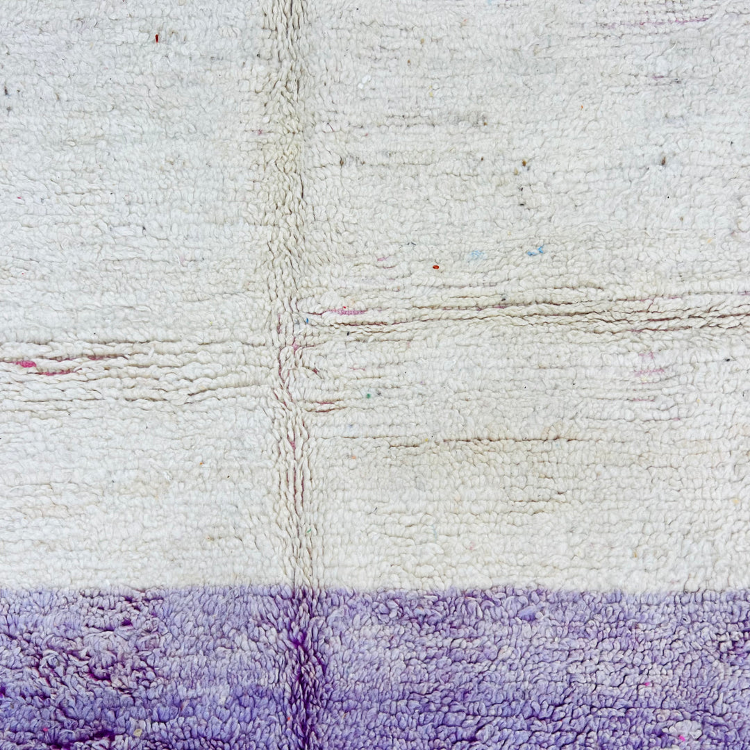 Close-up of a geometric vintage Moroccan rug with ivory and purple hues, showcasing hand-knotted wool texture.