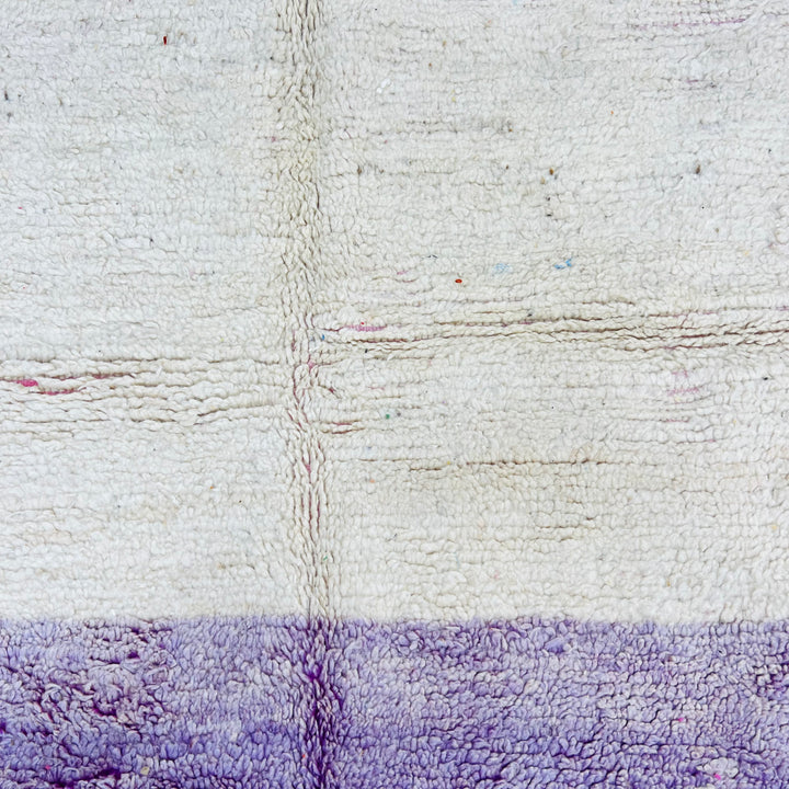 Close-up of a geometric vintage Moroccan rug with ivory and purple hues, showcasing hand-knotted wool texture.