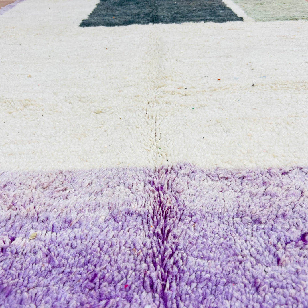 Close-up of a vintage Moroccan rug with geometric blocks in ivory, purple, and green tones, showcasing its plush wool texture.