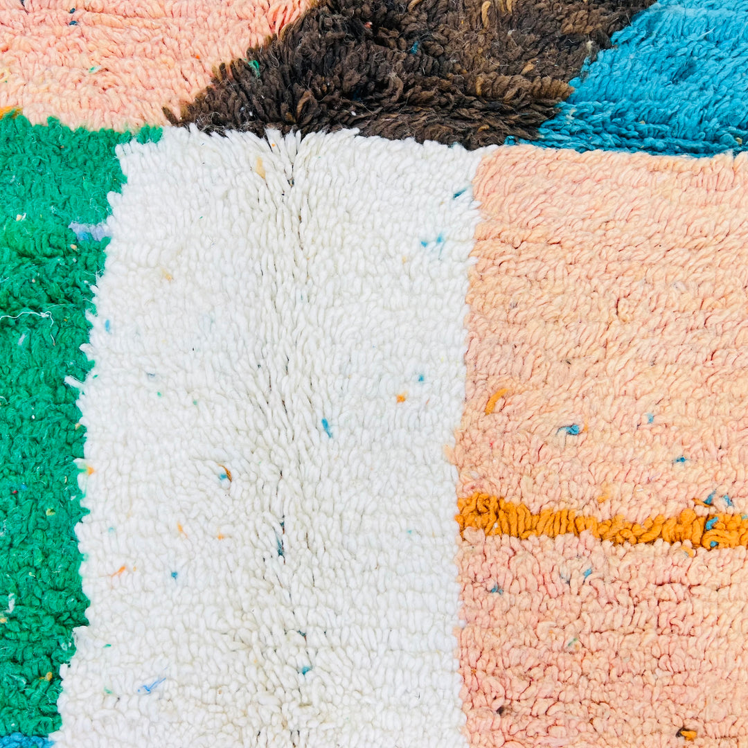 Close-up of a vintage Moroccan rug with colorful diagonal blocks of green, ivory, pink, and blue, handwoven by Berber artisans.