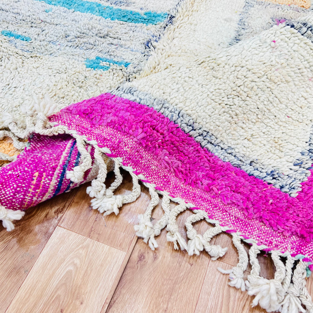 Close-up of a pink vintage Moroccan rug with intricate tribal patterns and fringe detailing on a wooden floor.