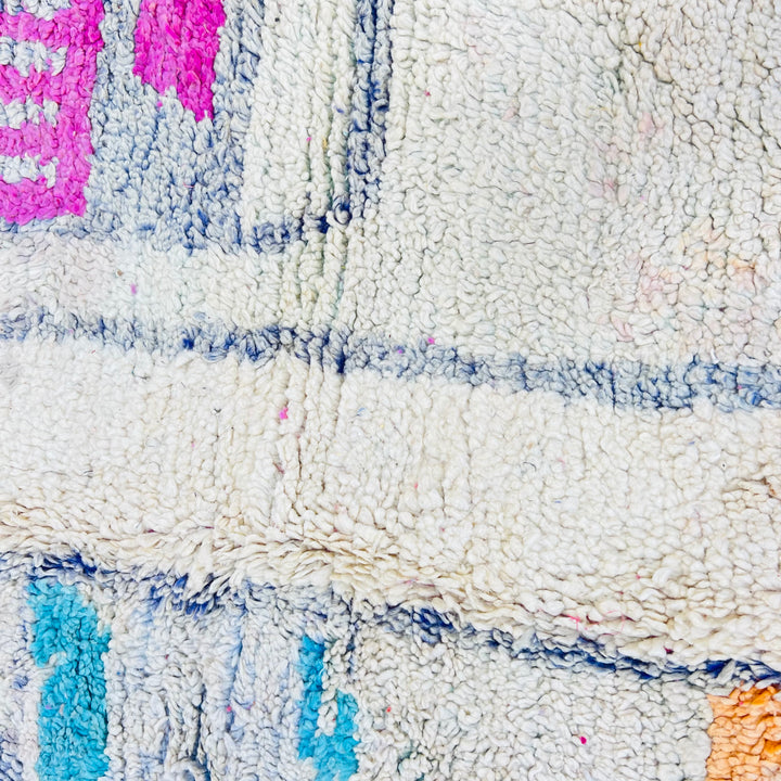 Close-up of pink vintage Moroccan berber rug with tribal patterns in cream, blue, and orange, showcasing intricate craftsmanship.