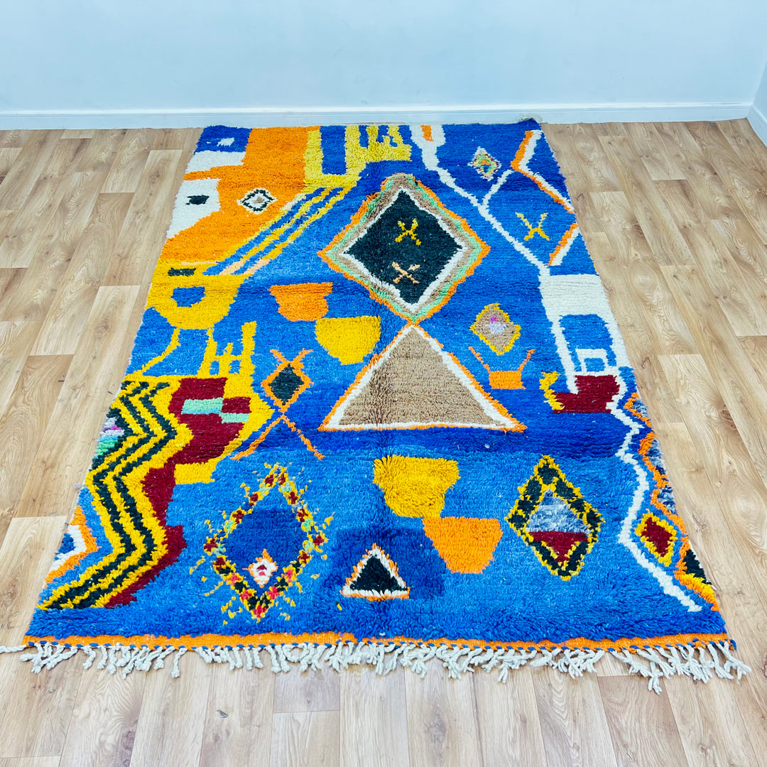 Blue vintage Moroccan rug with colorful Berber symbols including diamonds and pots on wooden floor; dimensions 257x160 cm.