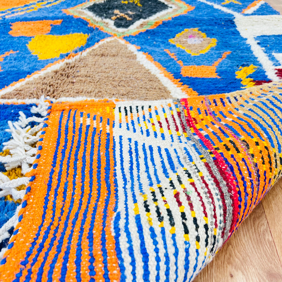 Close-up of a blue vintage Moroccan rug with tribal patterns, featuring cobalt blue, orange, black, and white colors.