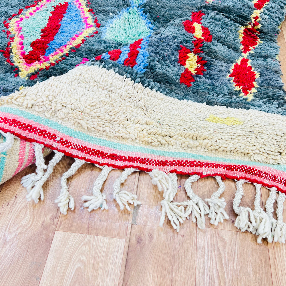 Vintage Moroccan rug with vibrant diamond patterns in red, yellow, blue on green background, featuring tribal motifs and tassels.
