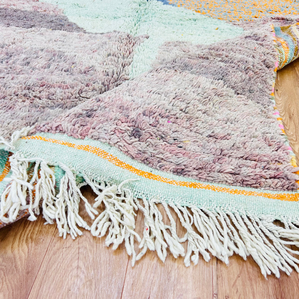 Abstract Moroccan wool rug with earthy hues and fringe, showcasing traditional craftsmanship on wooden floor.