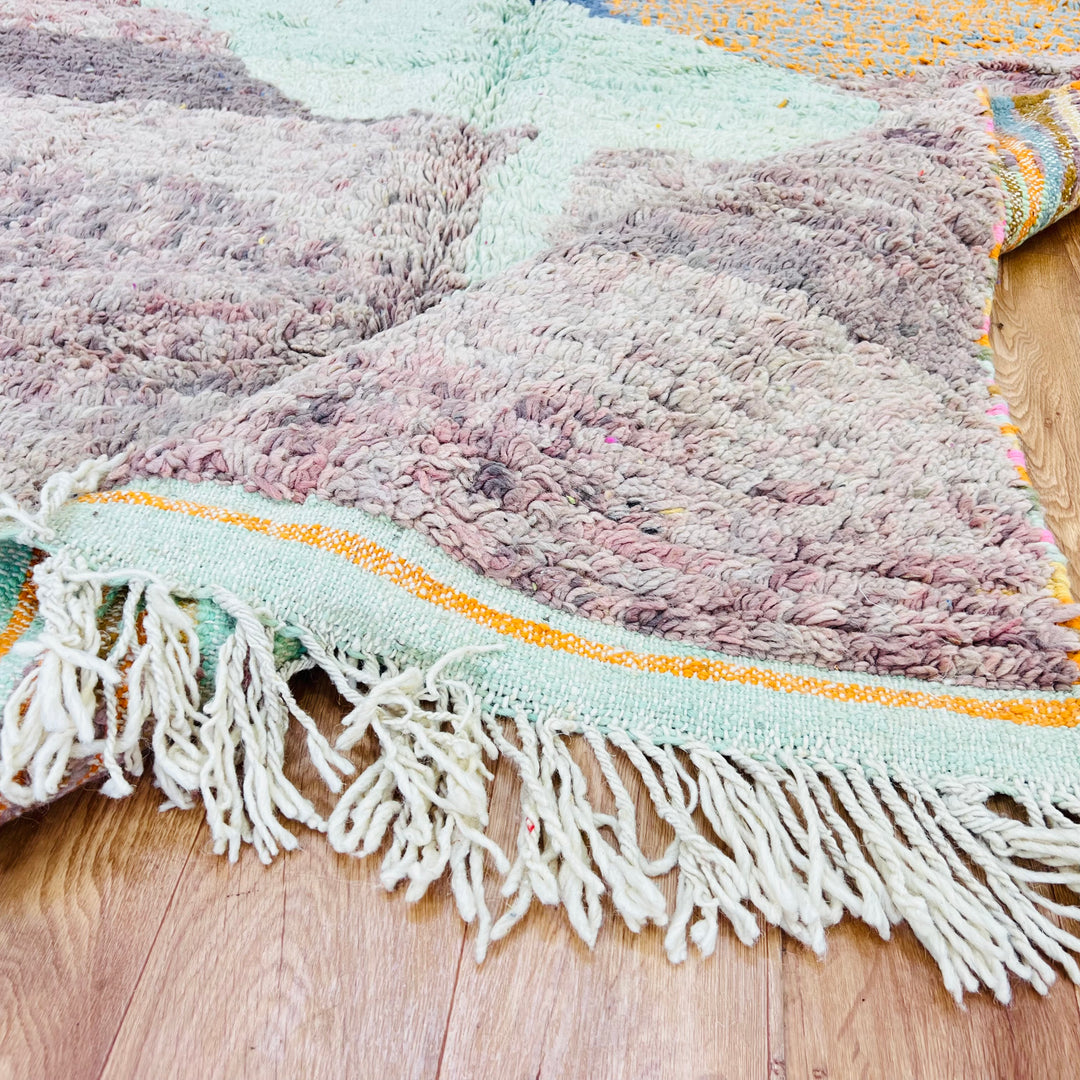 Abstract Moroccan wool rug with earthy hues and fringe, showcasing traditional craftsmanship on wooden floor.