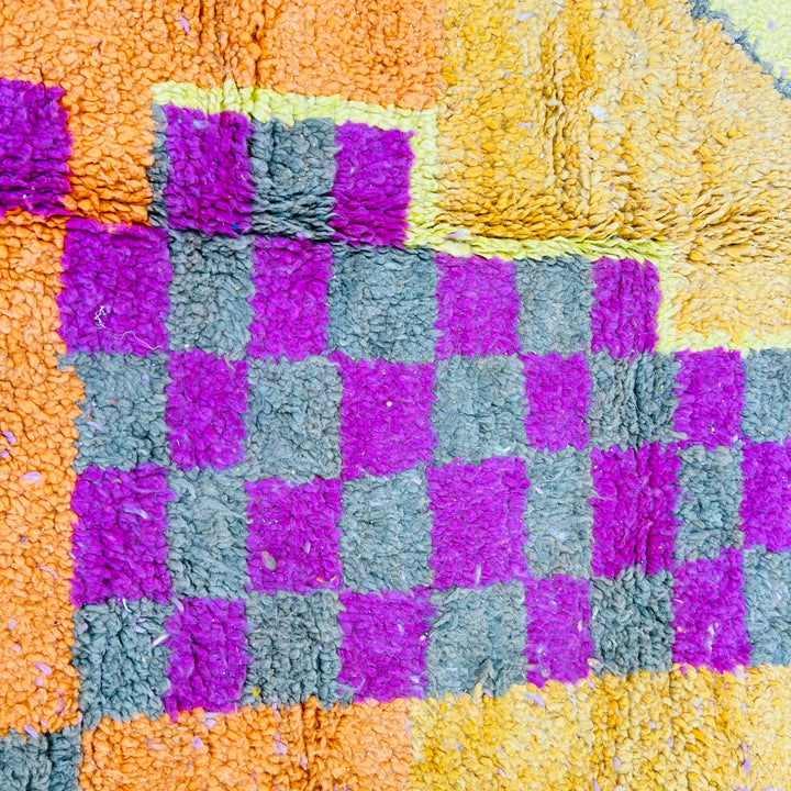 Close-up of a Moroccan Berber rug with orange, pink, yellow, and grey geometric checkerboard pattern, handcrafted by artisans.