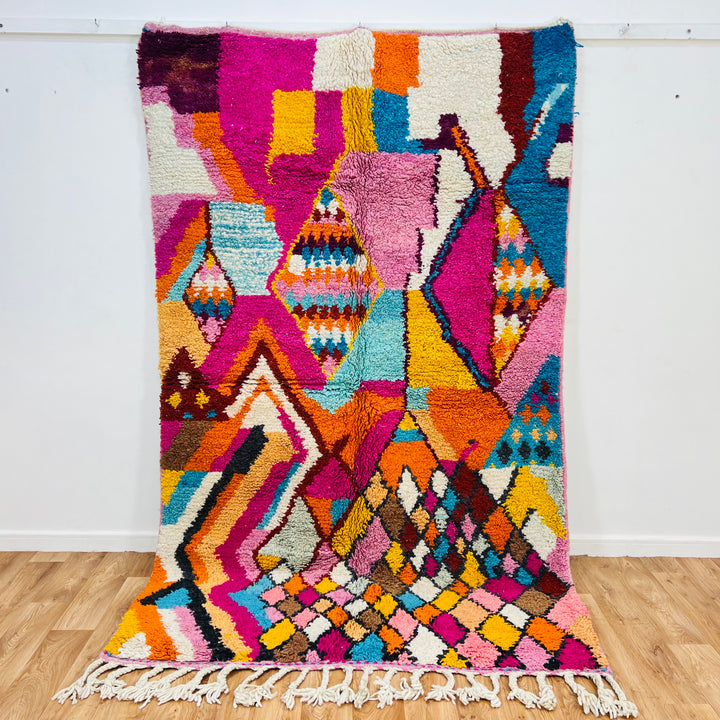 Colorful Moroccan Berber rug with vibrant pink, orange, turquoise, and yellow abstract patterns.