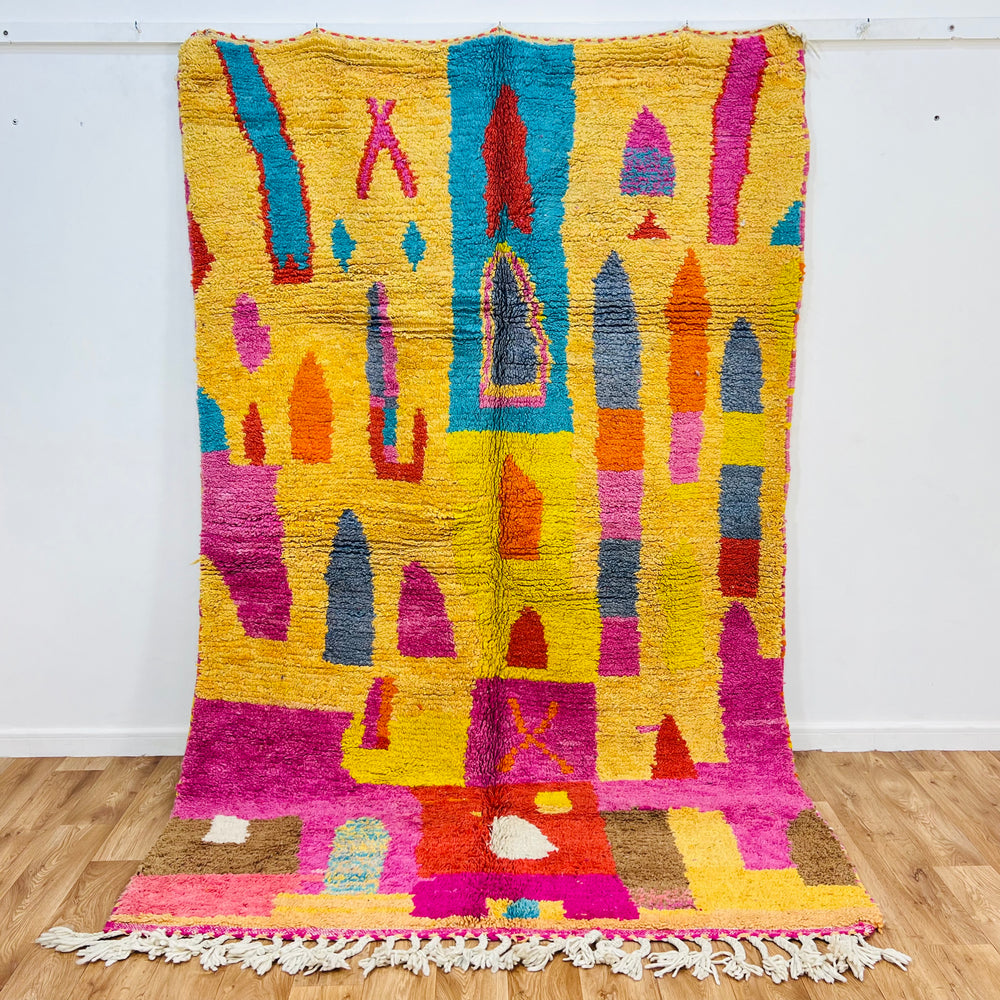 Colorful Moroccan shag rug with multicolored geometric patterns in yellow, pink, blue, and orange hues.
