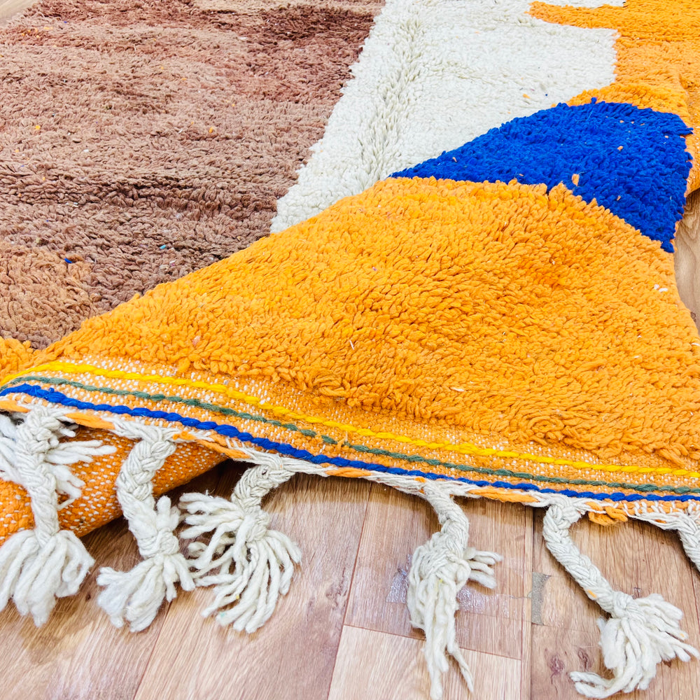 Colorful Moroccan wool rug with abstract motifs, showcasing vibrant yellow, orange, and blue hues. Handmade by Berber artisans.