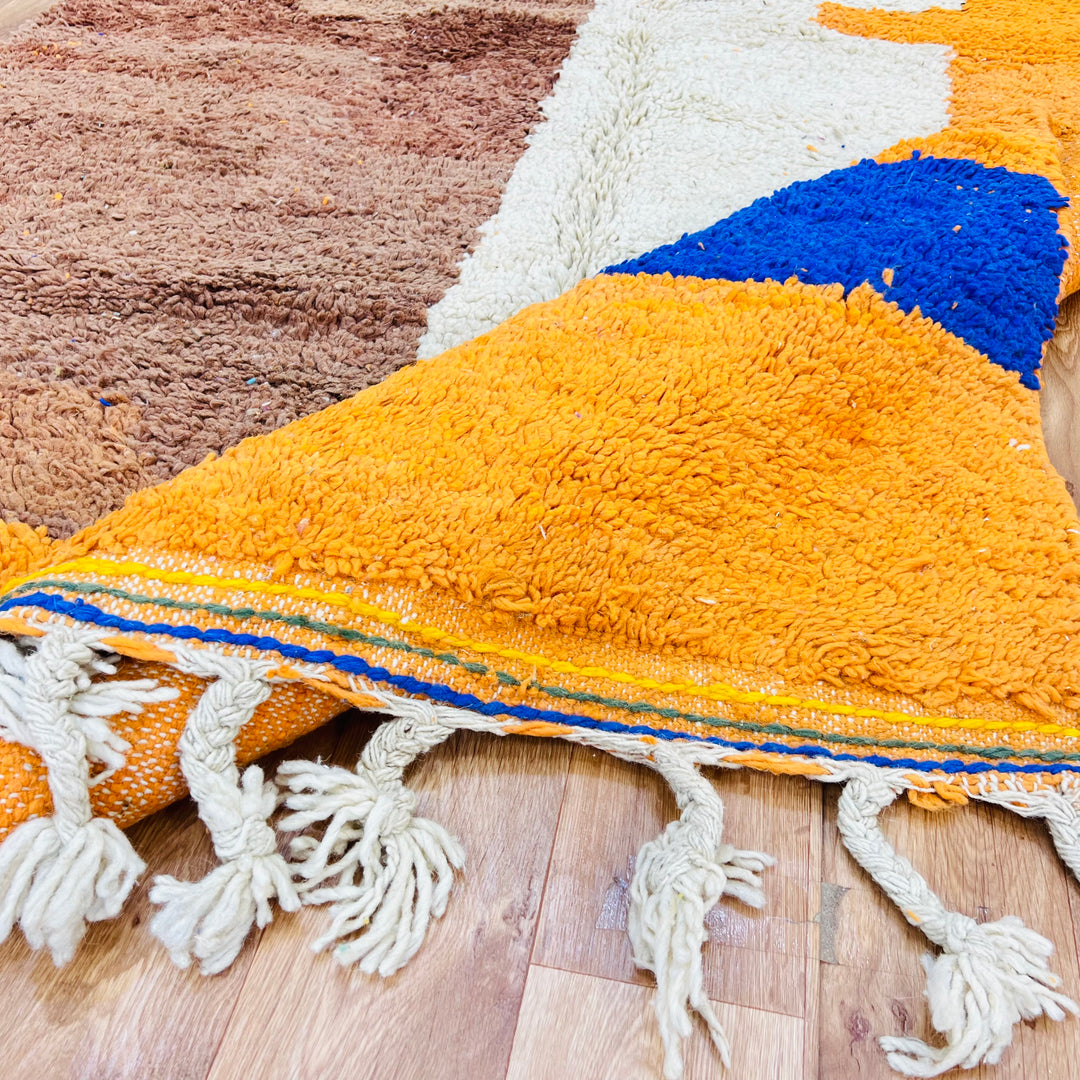 Colorful Moroccan wool rug with abstract motifs, showcasing vibrant yellow, orange, and blue hues. Handmade by Berber artisans.
