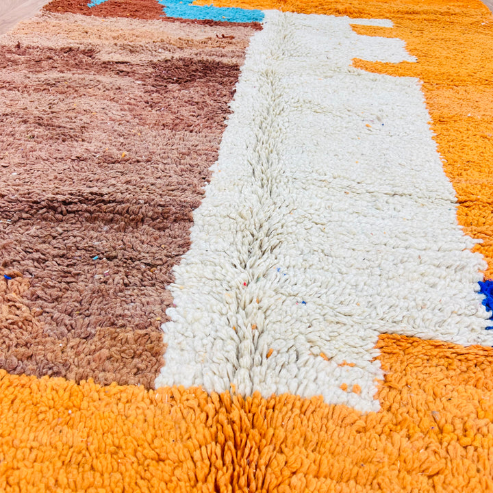 Colorful Moroccan rug close-up with vibrant abstract motifs in wool, handmade by Berber artisans, showcasing orange, brown, and white colors.