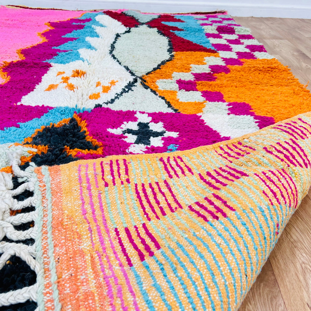 Colorful Moroccan wool rug with bold wavy stripes in red, yellow, aqua, pink, grey, and black; handwoven by Berber artisans.