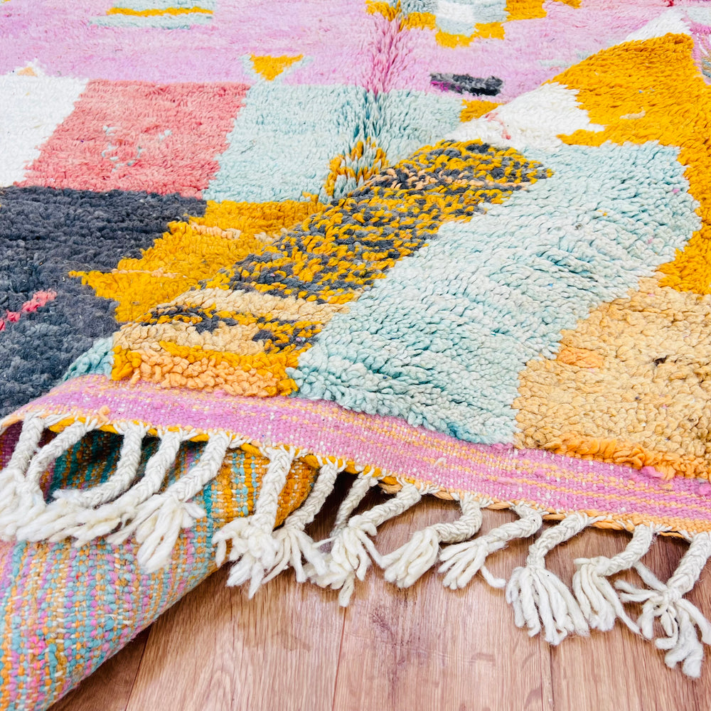 Close-up of a vintage pink Moroccan rug with colorful geometric patterns on wooden floor, featuring fringe detail.