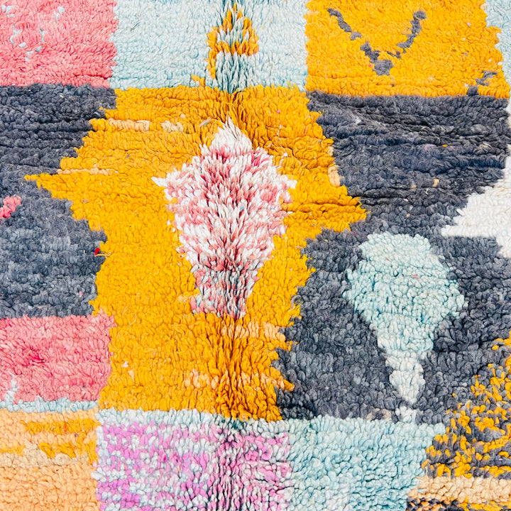 Close-up of colorful geometric patterns on a vintage pink Moroccan rug with yellow, gray, and blue accents, handmade by Berber artisans.
