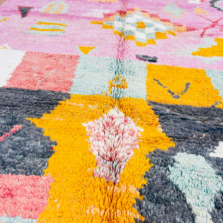 Close-up of a vintage pink Moroccan Berber rug with geometric and tribal patterns in orange, mint, and sunset tones.
