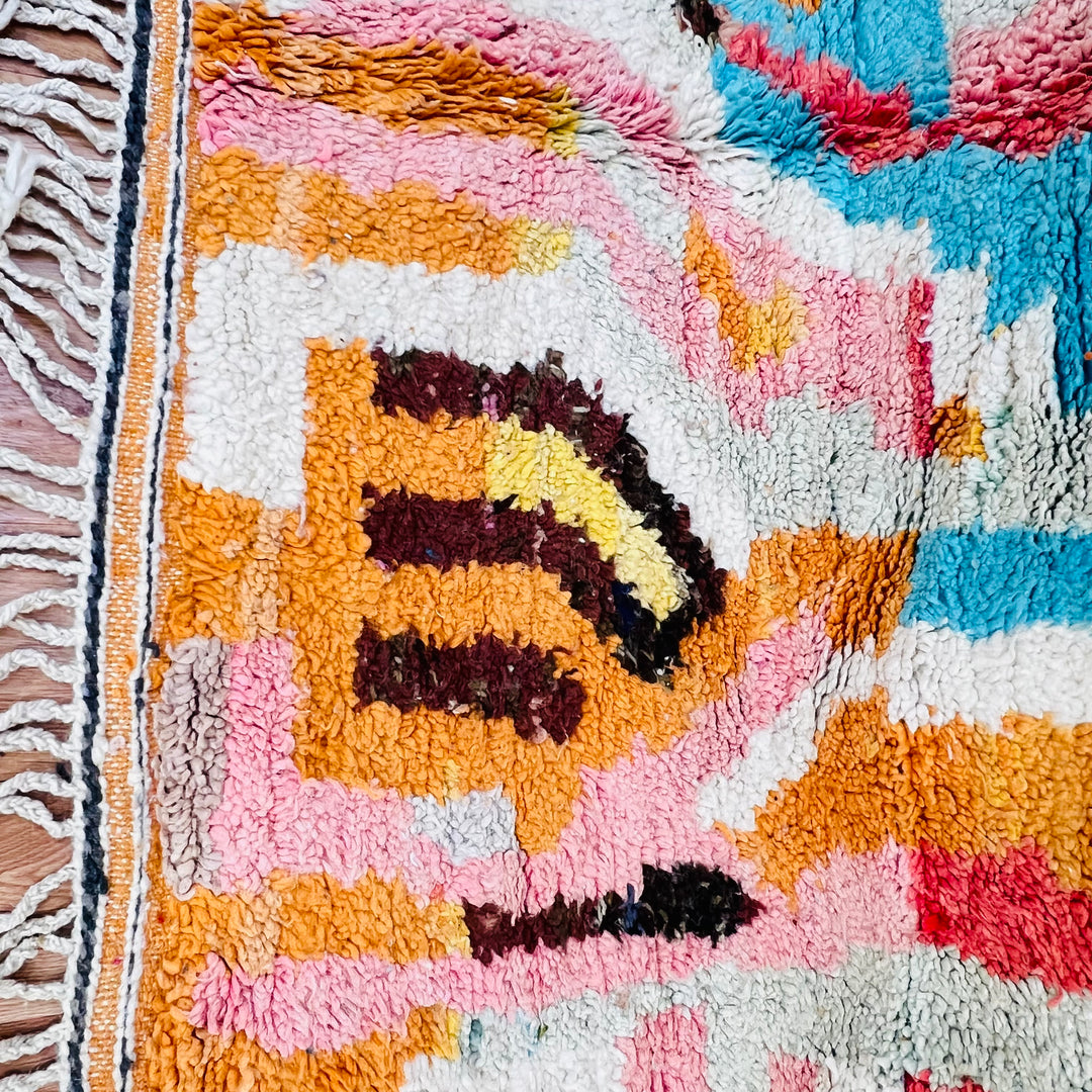 Colorful Moroccan wool rug with geometric pattern in orange, blue, red, pink, ivory, and chocolate tones. Traditional weaving.