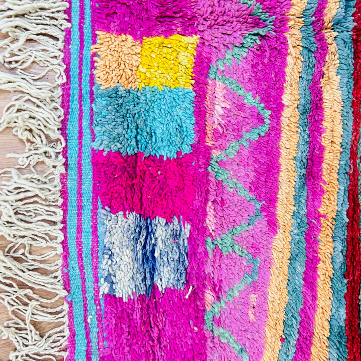 Colorful Moroccan Berber wool rug with geometric patterns in red, yellow, blue, and pink. Handmade in the Middle Atlas Mountains.