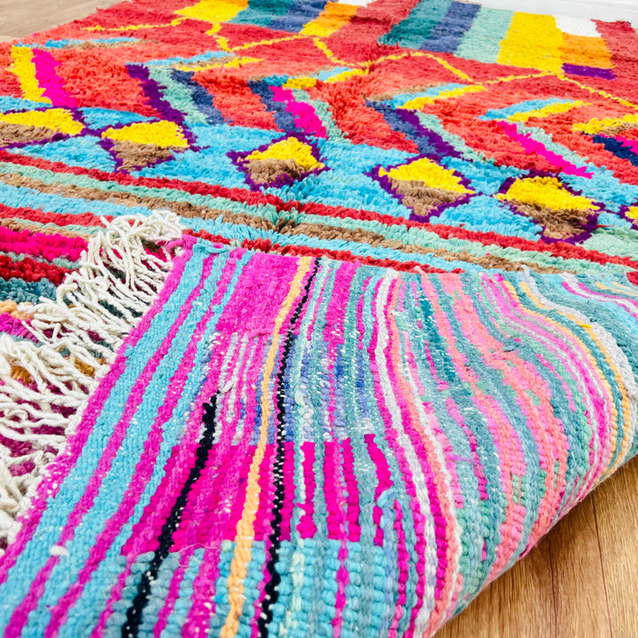 Colorful Moroccan Berber wool rug with vibrant geometric patterns, featuring reds, yellows, blues, and pinks. Handmade tribal art.