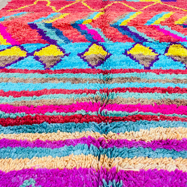 Colorful Moroccan Berber rug with vibrant geometric patterns, handmade wool, 9x4.9 ft, featuring reds, blues, yellows, and pinks.