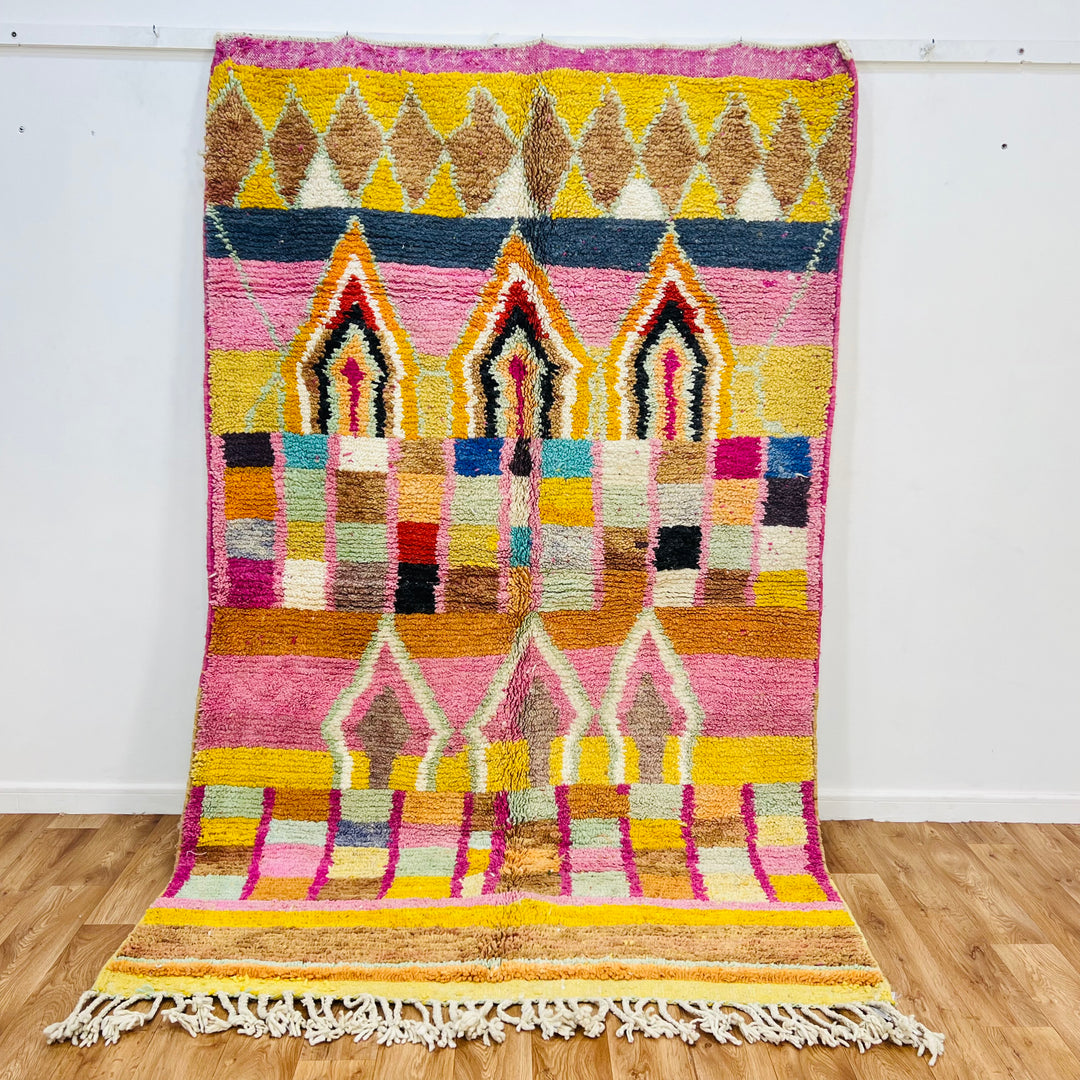 Colorful Moroccan wool rug with diamond and arch motifs, featuring pink, yellow, and natural tones. Moroccan Berber carpet.