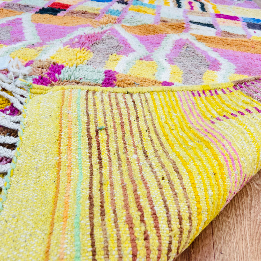 Colorful Moroccan wool rug with geometric designs in yellow, pink, and natural tones. Handwoven traditional Berber carpet.
