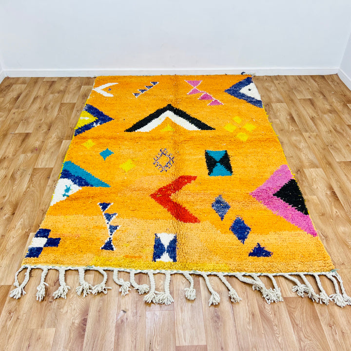 Orange Moroccan wool rug with tribal Berber motifs in black, pink, blue. Handmade textured surface, 246x167cm.