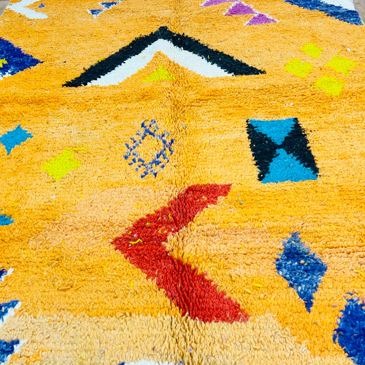 Orange Moroccan wool rug with vibrant tribal Berber motifs in black, pink, blue, red, yellow, and ivory, handmade in traditional style.