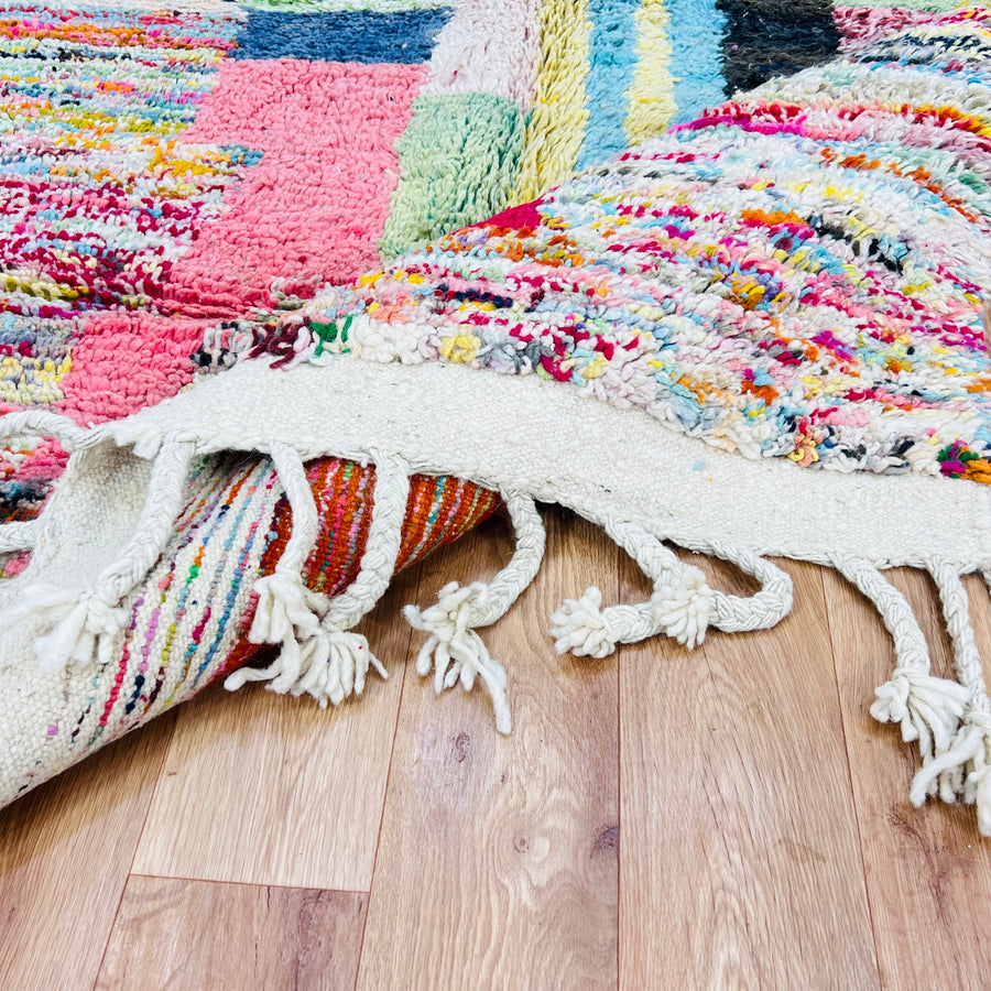 Colorful Moroccan Berber Wool Rug with vibrant abstract patterns and tassels, showcasing traditional craftsmanship on wooden floor.