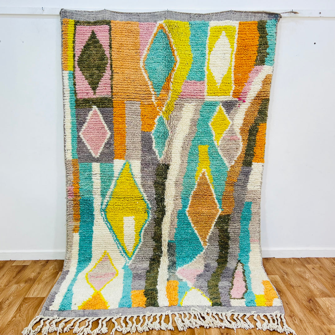 Colorful Moroccan wool rug with diamond patterns in orange, teal, yellow, blush pink; traditional Berber design.
