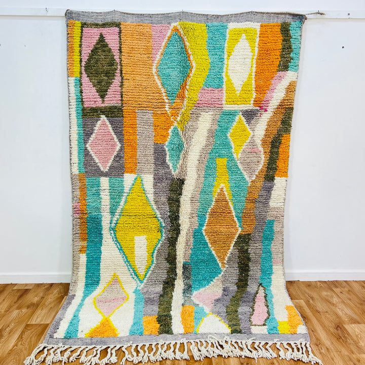 Colorful Moroccan wool rug with diamond patterns in orange, teal, yellow, blush pink; traditional Berber design.
