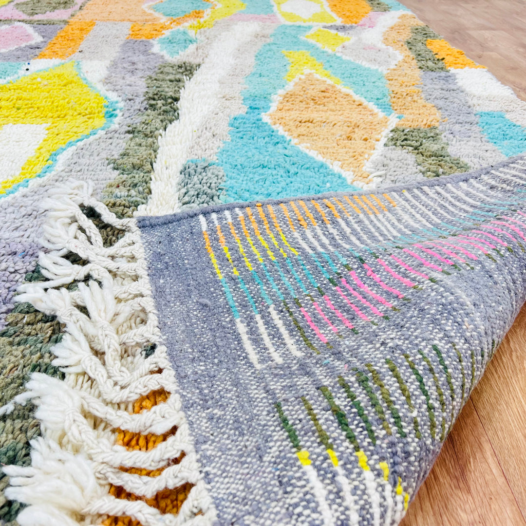Colorful Moroccan wool rug with orange, teal, yellow, and pink diamond patterns, showing texture and fringe detail.