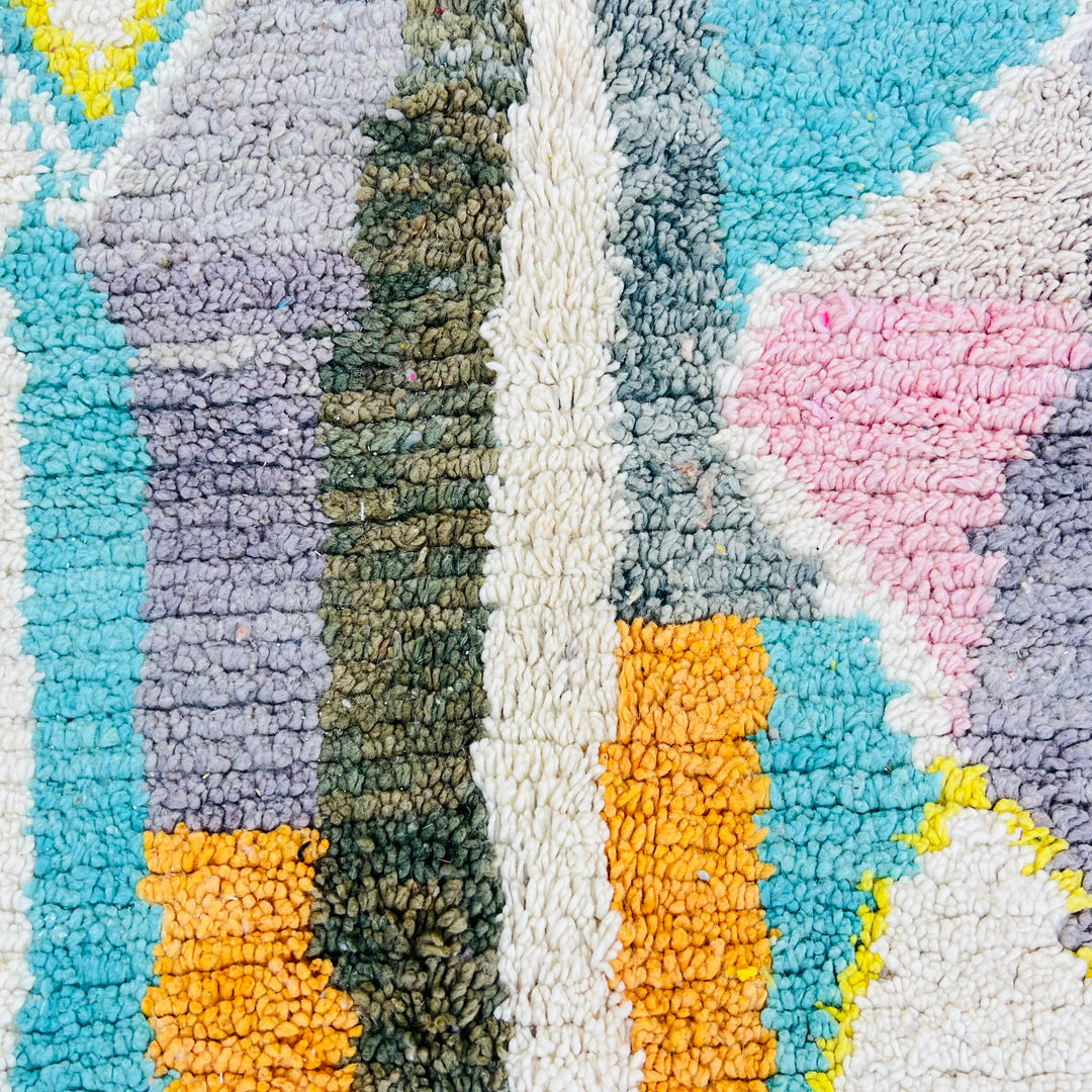 Colorful Moroccan wool rug with diamond patterns in orange, teal, yellow, and blush pink. Handmade using traditional Berber techniques.