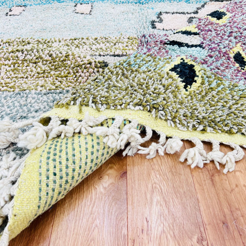 Colorful vintage Moroccan rug with abstract geometric patterns and fringed edges on a hardwood floor.