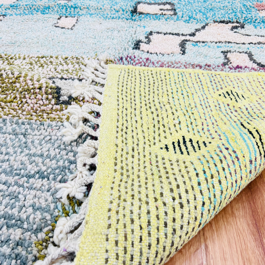 Close-up of a vintage Moroccan rug showing handwoven colorful Berber patterns and intricate textures on wooden floor.