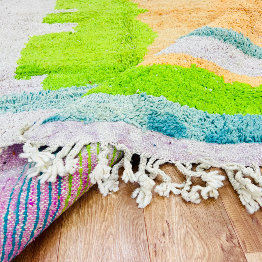 Handmade Moroccan wool rug with vibrant colors and geometric design, featuring lime green, orange, and ivory tones on a hardwood floor.