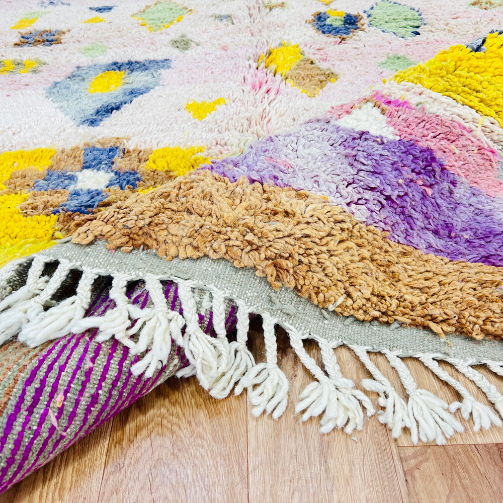Close-up of a handwoven pink and yellow vintage Moroccan rug with Berber motifs, showcasing plush texture and fringe on wooden floor.