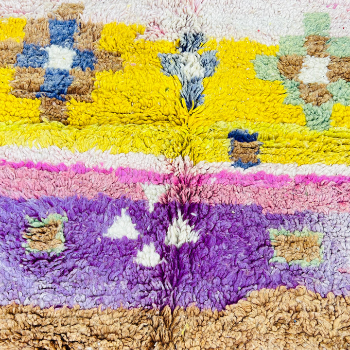 Vintage Moroccan rug with pink, yellow, and turquoise Berber motifs. Handwoven wool texture.
