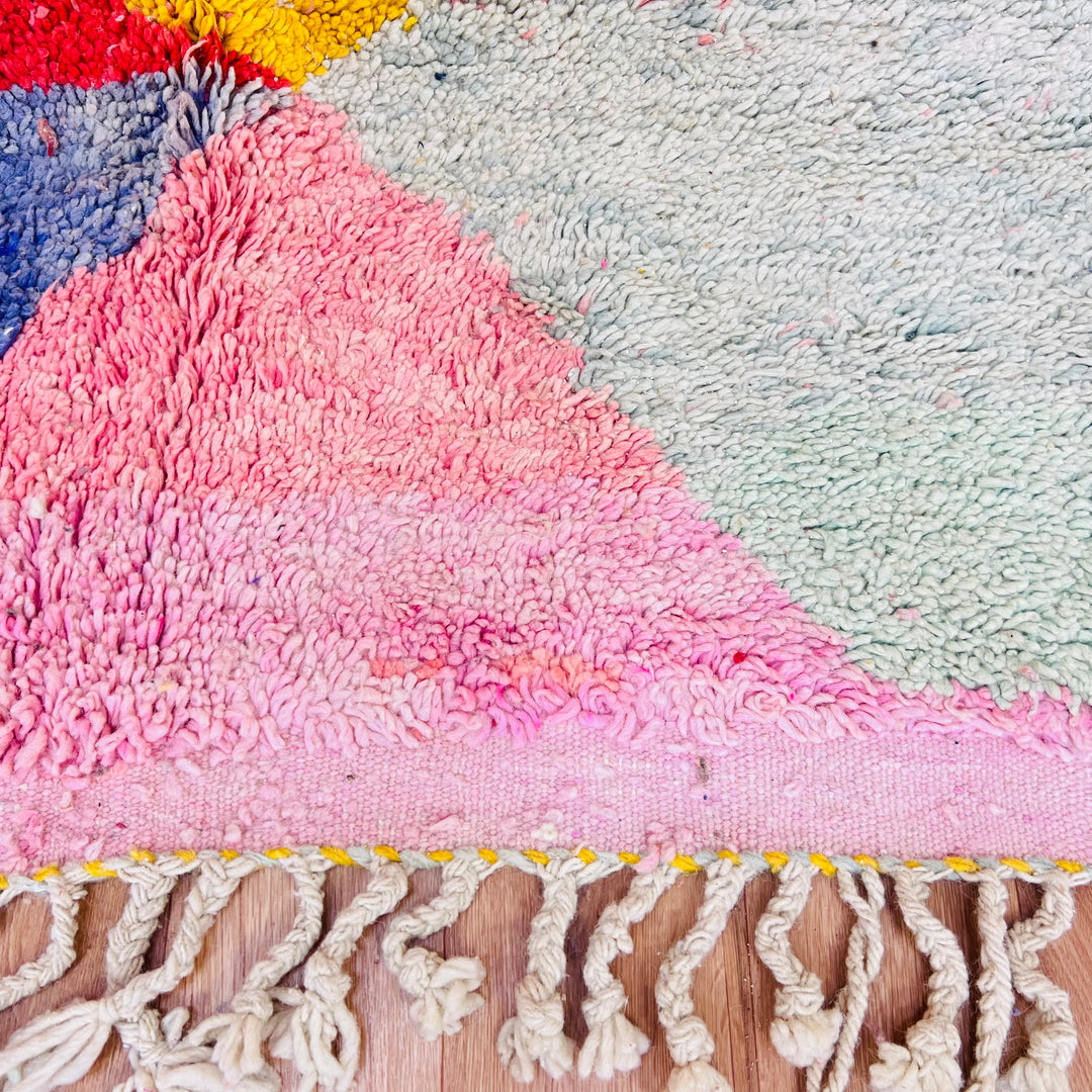 Close-up of a handmade pink Moroccan rug with diamond patterns and colorful fringes, showcasing vibrant Moroccan Berber design.