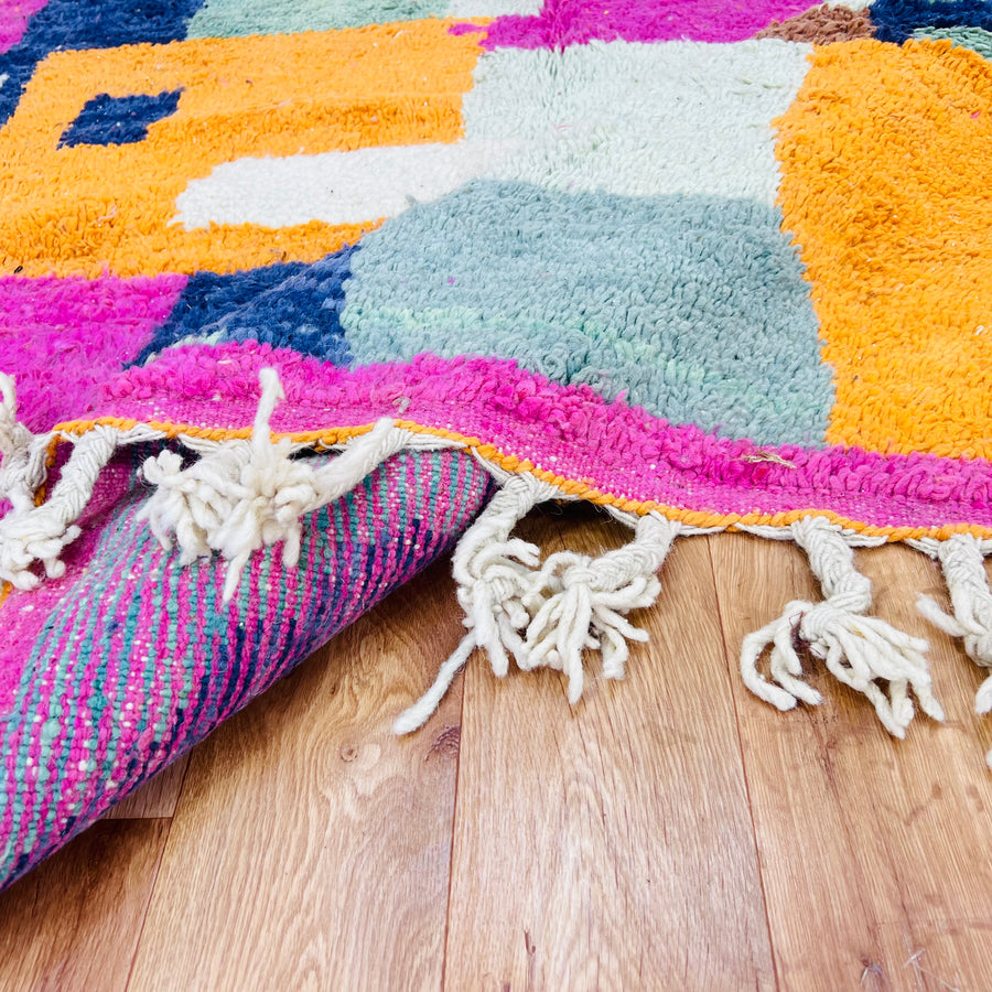 Handwoven colorful abstract Moroccan shag rug with vibrant geometric patterns in pink, orange, blue, and mint on hardwood floor.