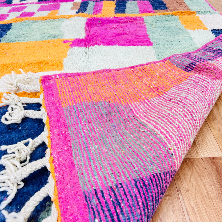 Colorful abstract vintage Moroccan rug with vibrant geometric patterns in fuchsia, orange, blue, and earthy tones, perfect for home decor.