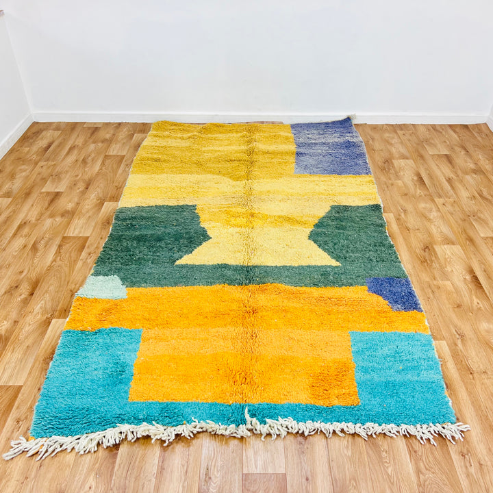 Yellow and green abstract Moroccan rug with geometric pattern on wooden floor, 100% wool, handmade by artisans in Atlas Mountains.